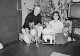 grayscale photo of boy sitting beside dog on floor