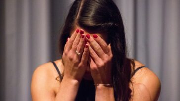 woman in black tank top covering her face with her hands