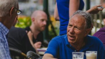man in blue polo shirt talking to man while drinking coffee