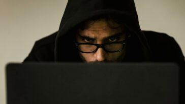 Serious young male programmer wearing black hoodie browsing netbook and hacking software in studio