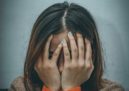 woman in brown sweater covering her face with her hand