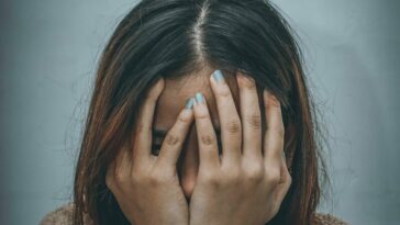 woman in brown sweater covering her face with her hand
