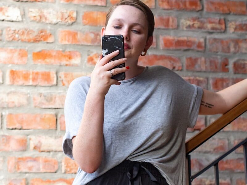 woman in gray crew neck t-shirt and black skirt holding black smartphone