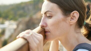 A thoughtful woman leans on a railing, lost in deep contemplation outdoors.