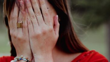 Woman covering her face with hands in an emotional moment outdoors.