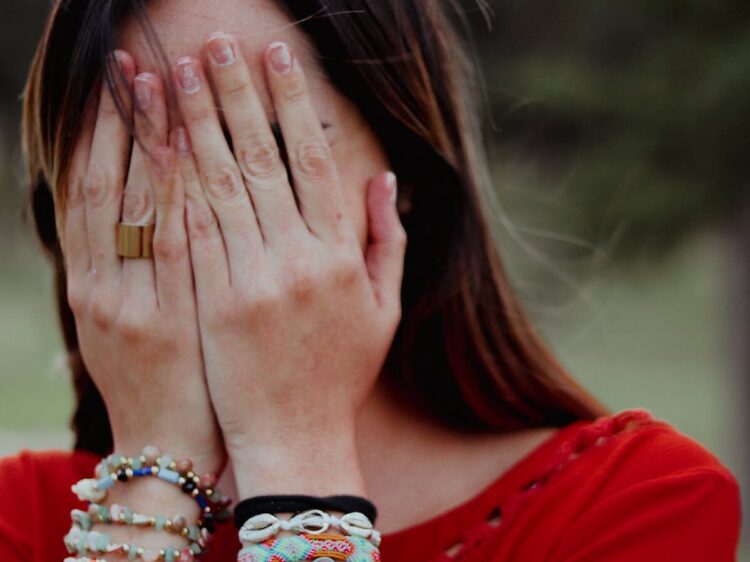 Woman covering her face with hands in an emotional moment outdoors.