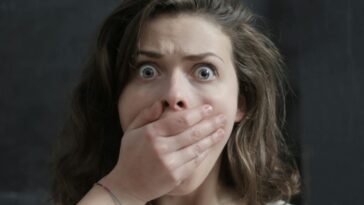 Close-up of a woman with a shocked expression, covering her mouth with her hand. Emotional and intense moment.