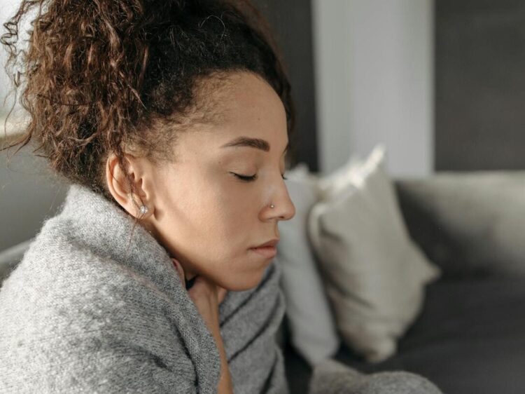 Young woman resting at home, wrapped in a blanket and feeling unwell, conveying a sense of illness or discomfort.