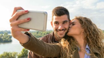 A happy couple taking a romantic selfie by the scenic riverside on a sunny day.