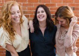 three women standing next to each other in front of a brick wall