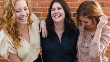 three women standing next to each other in front of a brick wall