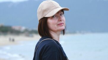 Woman with cap smiling by the beach in Sabaudia, Italy, with mountains in the background.