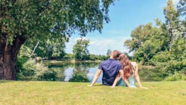 A couple sitting by a lake enjoying a sunny day in a lush park.