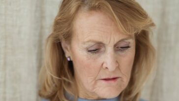 Pensive senior woman in blue sweater looking down, expressing thoughtful and serene mood indoors.