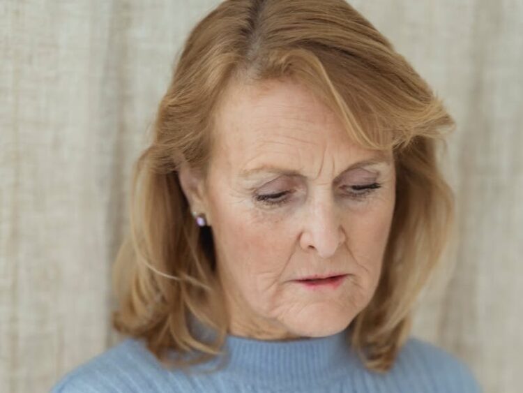 Pensive senior woman in blue sweater looking down, expressing thoughtful and serene mood indoors.