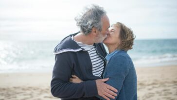 A senior couple shares a romantic kiss on a sunny beach in Portugal, embodying love and companionship.