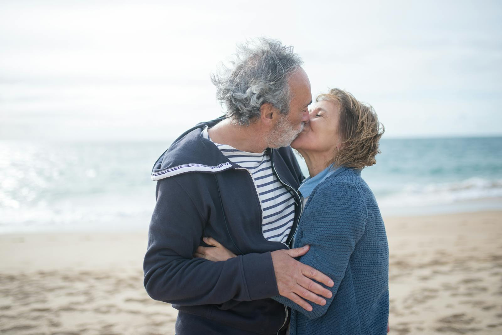 A senior couple shares a romantic kiss on a sunny beach in Portugal, embodying love and companionship.