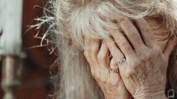 Senior woman in a thoughtful pose with hands covering face, expressing emotion.