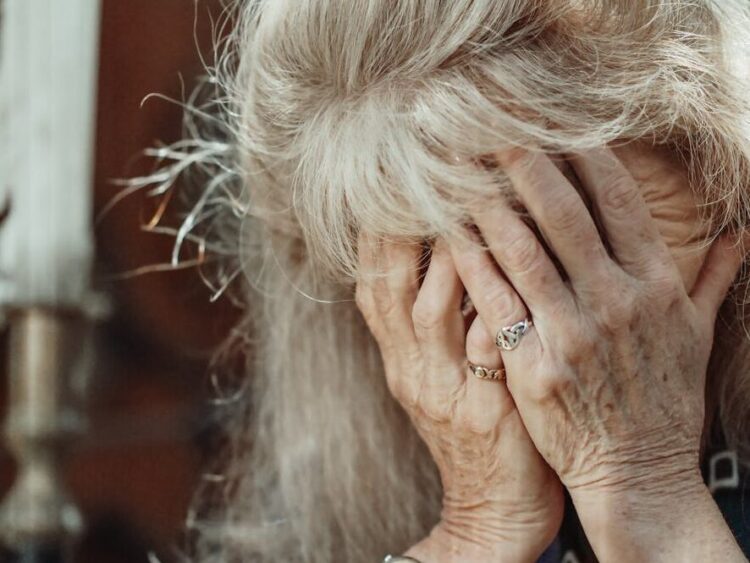 Senior woman in a thoughtful pose with hands covering face, expressing emotion.