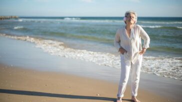 Senior woman in headphones enjoys music on a sunny Portuguese beach.