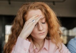 Stressed woman with red hair in pink shirt facing work pressure. Indoor office scene.