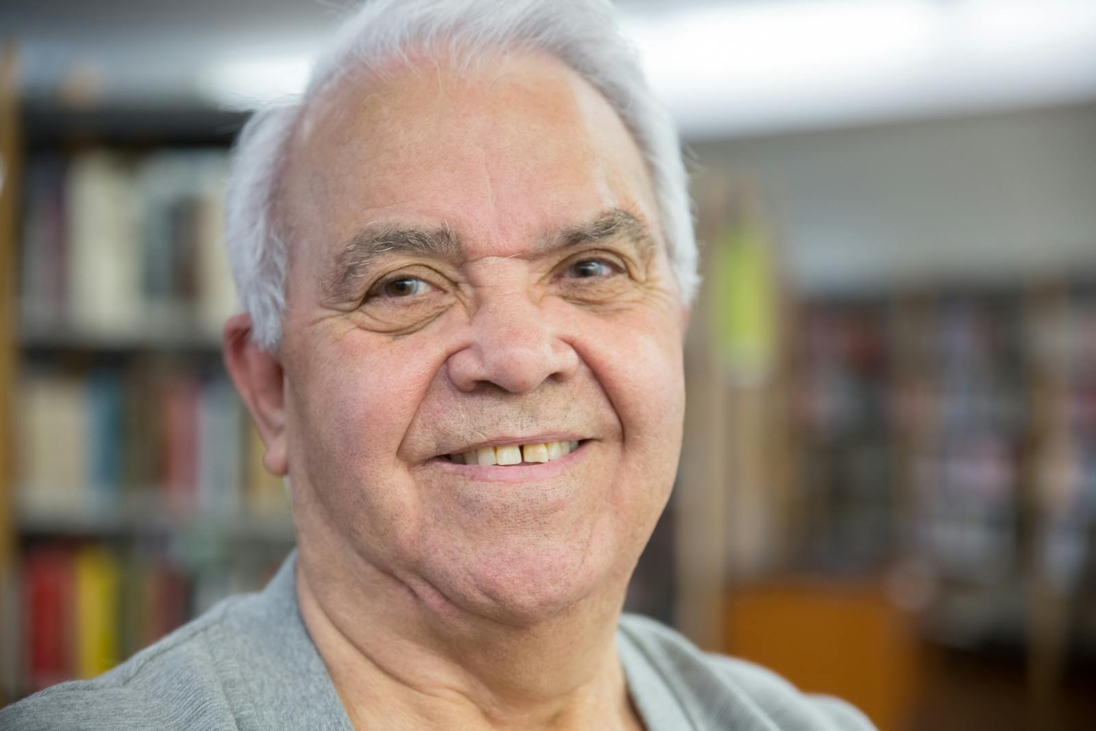 Close-up of a senior man with white hair smiling warmly in a library setting.