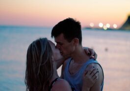 A couple shares a romantic kiss at the beach during sunset, capturing love and intimacy.