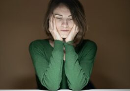 Thoughtful woman in green sweater looking down in low light setting.