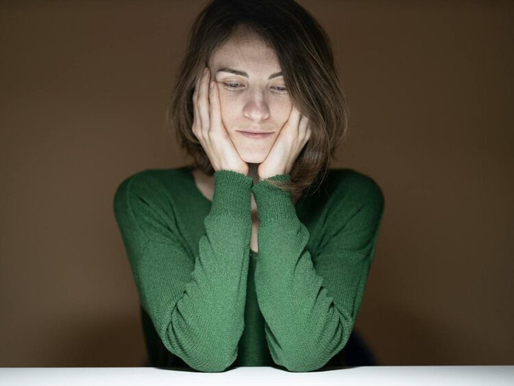 Thoughtful woman in green sweater looking down in low light setting.