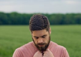 man in pink long sleeve shirt standing on green grass field during daytime