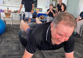 Senior man balancing on a fitness ball during an exercise class with peers.