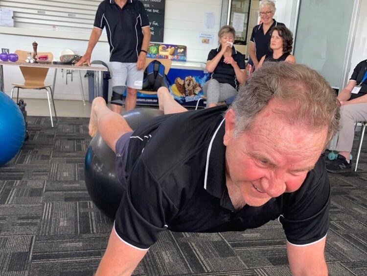 Senior man balancing on a fitness ball during an exercise class with peers.