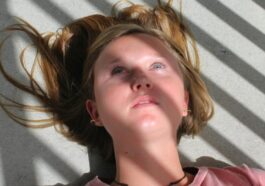 Close-up of a young woman lying on a floor with dramatic shadows and sunlight casting across her face.