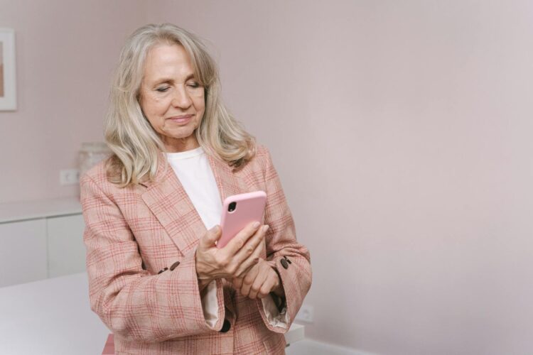 Elderly woman in plaid blazer using a smartphone indoors, looking content.