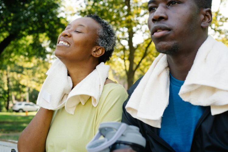 Two adults resting on a park bench after exercise, enjoying a serene outdoor setting.