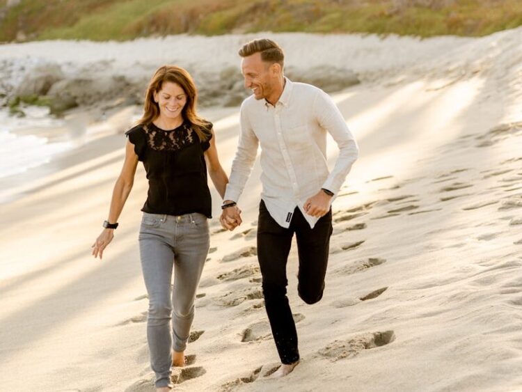 man in white dress shirt and woman in black dress walking on beach during daytime
