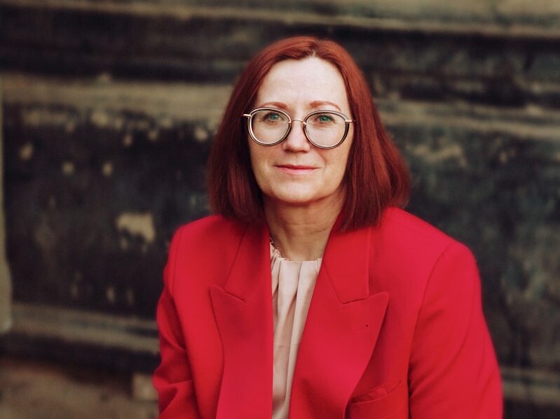 a woman in a red suit sitting on a tree stump