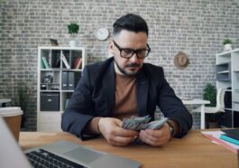 a man sitting at a table with a laptop and money