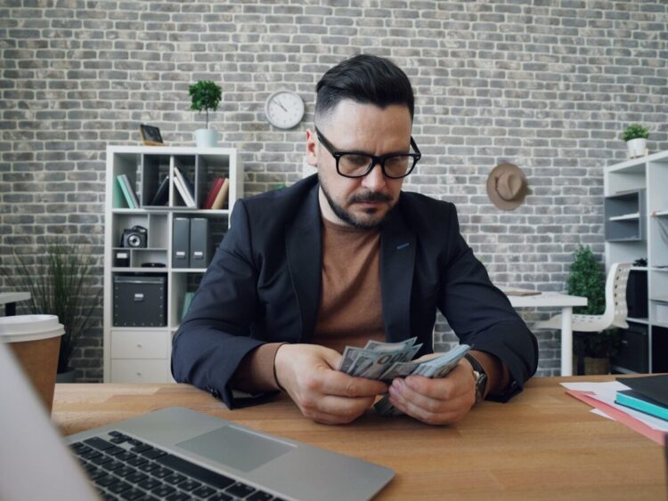 a man sitting at a table with a laptop and money