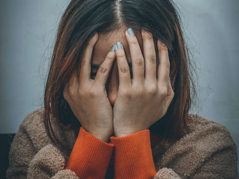 woman in brown sweater covering her face with her hand