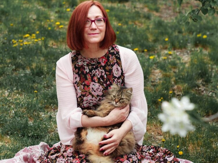 woman in white cardigan sitting on pink textile on green grass field during daytime
