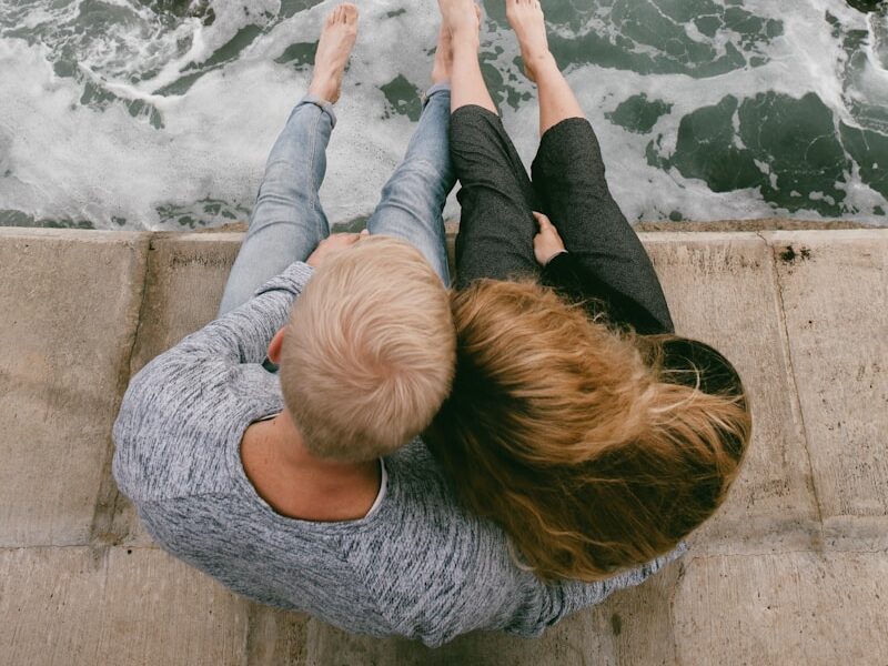man and woman sitting on cliff near body of water