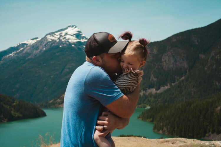 A heartwarming scene of a father hugging his daughter in a stunning mountain landscape.