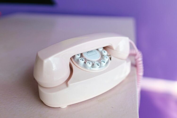 A classic off-white rotary phone on a pink table against a purple background.