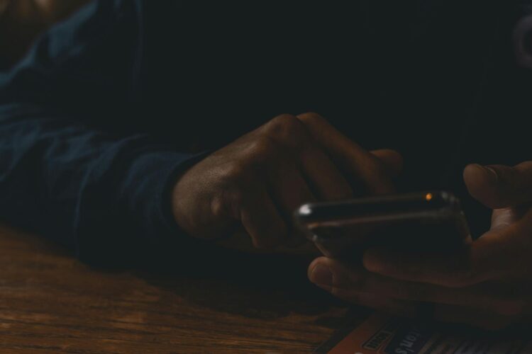 A close-up view of hands interacting with a smartphone in a dim indoor setting, highlighting technology use.