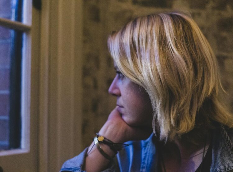 Contemplative adult woman with blonde hair looking out a window in Sydney, Australia.