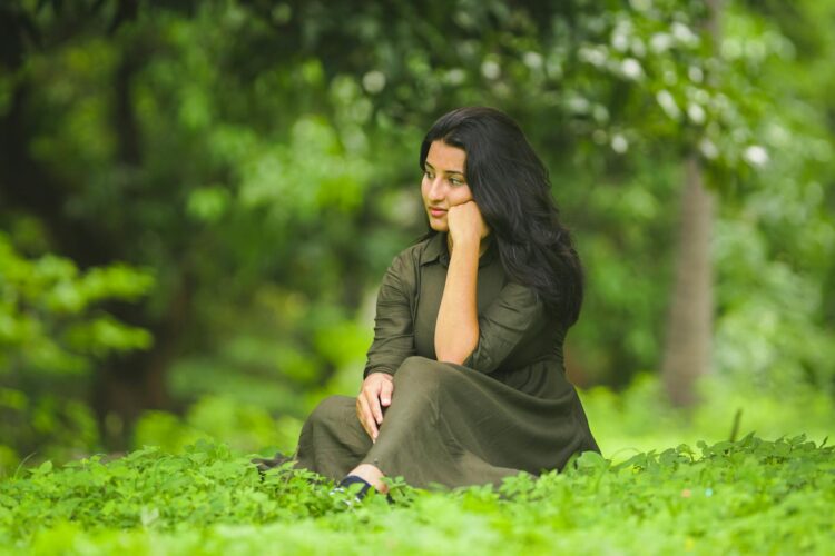 A serene image of a woman in a green dress sitting thoughtfully in a lush park.