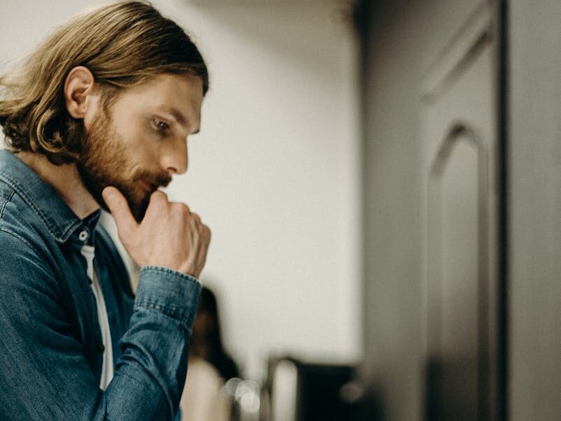 A man in deep thought while operating a printer in an office setting.