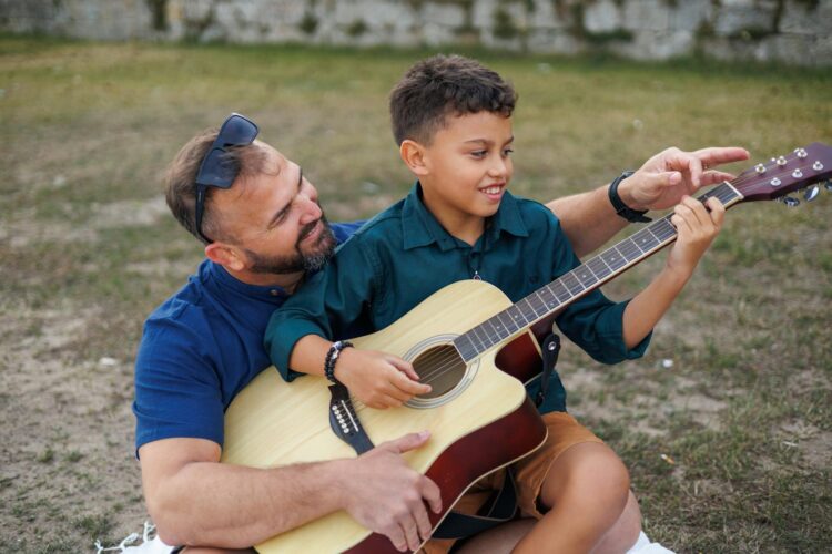 A father and son bonding over guitar lessons in a scenic outdoor setting.