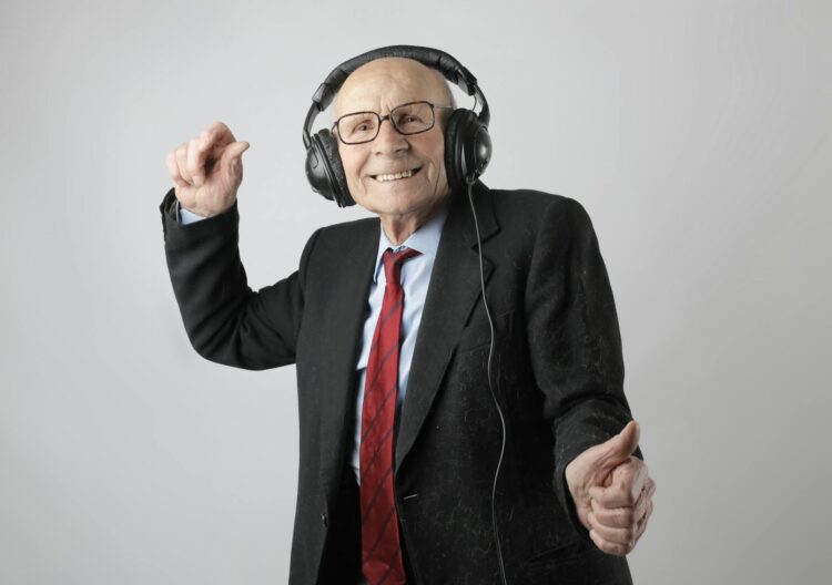 Happy senior man in formal attire delighting in music with headphones on a white background.